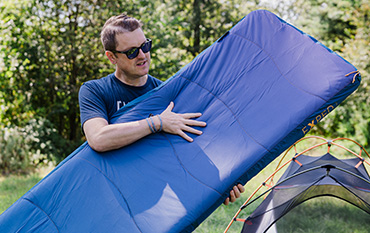 man holding sleeping pad at campsite
